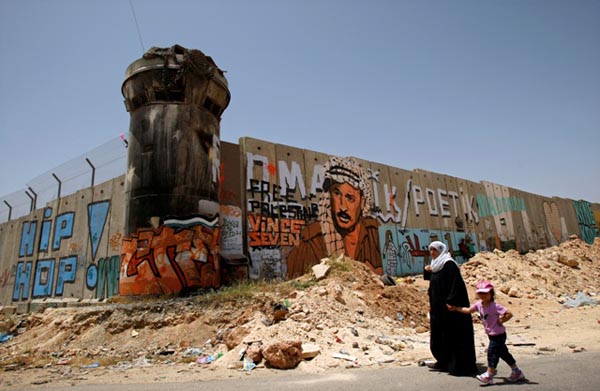 Foto: Vrouw en kind lopen langs Apartheidsmuur met graffiti