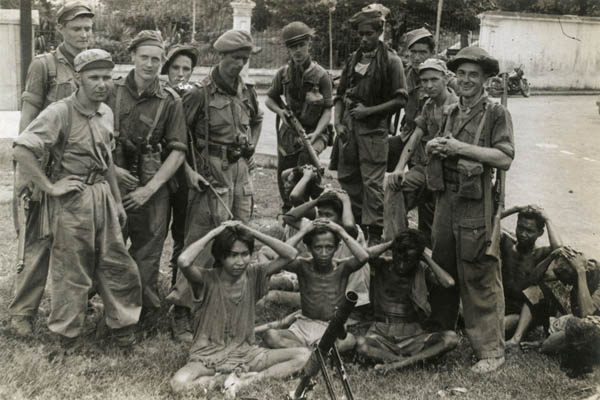 Foto van Nederlnadse militairen die Inodnesische gevangenen lachend onder schot houden.