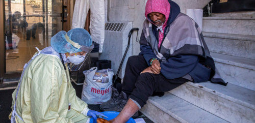 COVID-beschermde verpleegster helpt dakloze op trap buiten aan de voet