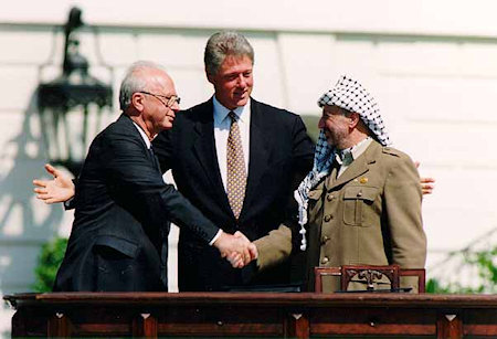 Rabin en Arafat schudden handen, Clinton met gespreide armen in het midden.
