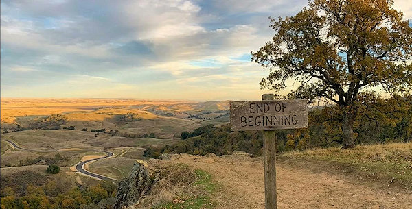 Zandweg op heuvel met bordje End of Beginning. Op de achtergrond een nieuwe weg, maar is die bereikbaar?